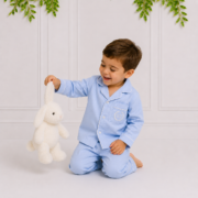 Boy wearing blue cotton pyjamas holding a white plush bunny by its ear while laughing in an elegant children's studio by Koco Bino.