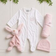 Baby girl hamper with a white babygrow, pink beanie, interlock cotton blanket and soft bunny comforter on an elegant flat lay.