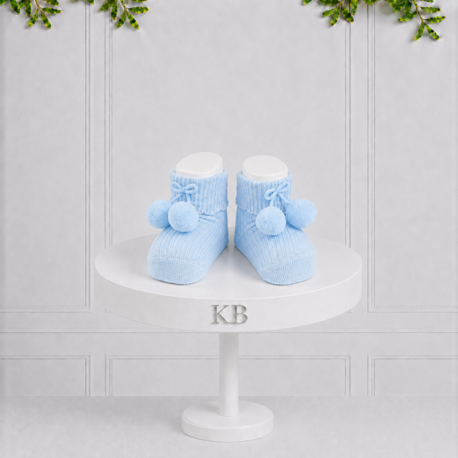 Light blue knitted baby socks with pom-pom details and turn-down cuffs, designed to keep little feet warm in timeless style and comfort.