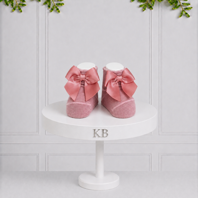 Dusty pink baby girl socks with elegant satin bows displayed on a white Koco Bino pedestal, perfect for special occasions and gifting.
