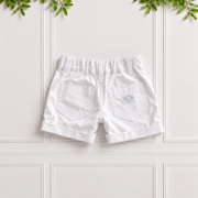 Boys white cotton sateen chino shorts with turned-up cuffs and back pockets, displayed against a white panelled background with green leaves.
