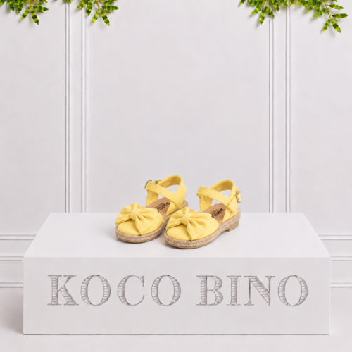 Lemon girls’ espadrille sandals with large bows and ankle straps displayed on a white Koco Bino pedestal with leafy greenery.