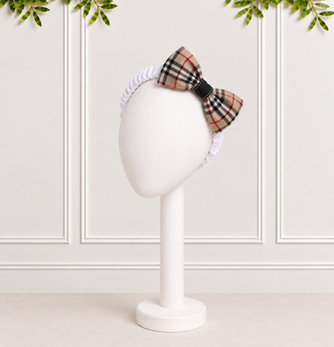 Baby girl bow headband featuring a stone tartan bow on a soft white ruched band, beautifully presented against a white panelled background.
