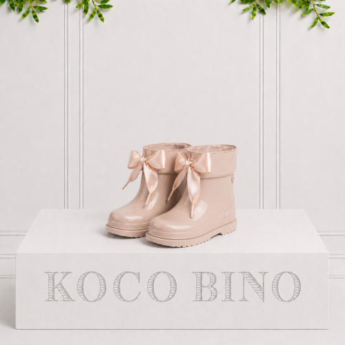 Elegant cream children's rain boots with satin ribbon bows, combining waterproof protection with classic style for little explorers.