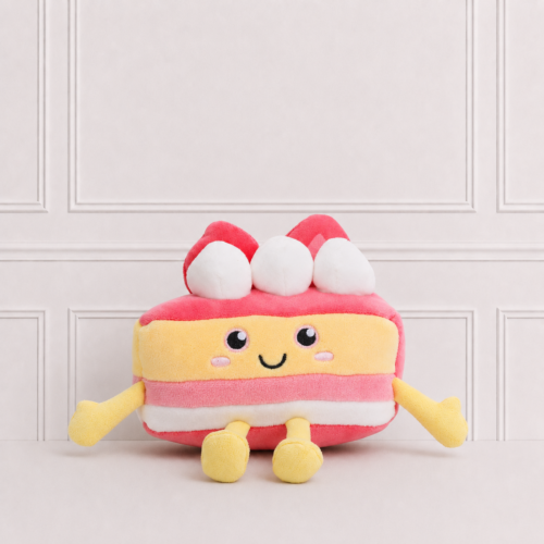 Soft strawberry cake plush toy with embroidered smiling face, cream layers and strawberries on top, displayed on a neutral background for décor.