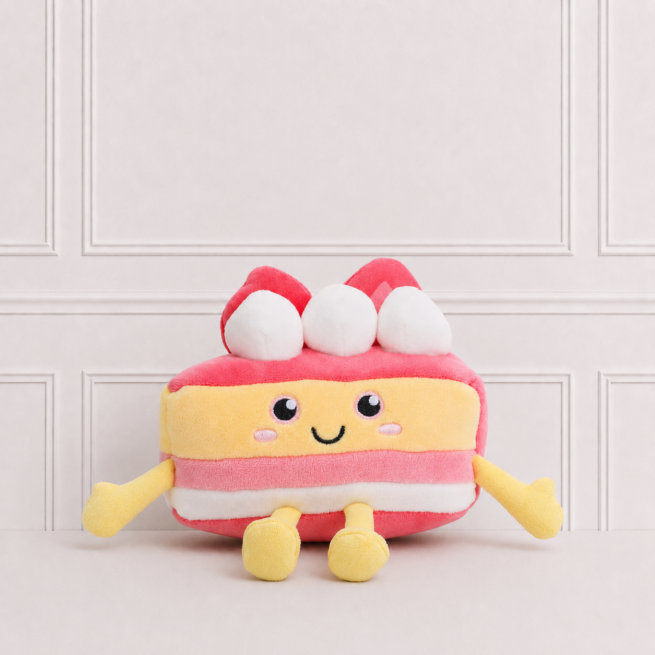 Soft strawberry cake plush toy with embroidered smiling face, cream layers and strawberries on top, displayed on a neutral background for décor.