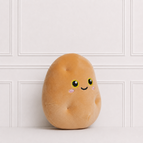Cute potato soft toy with a smiling embroidered face and soft plush fabric, displayed on a white surface against a classic white panelled backdrop.