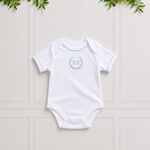 White baby bodyvest in soft cotton interlock with light blue piping, light blue KB embroidery and envelope neckline on a classic Koco Bino background.