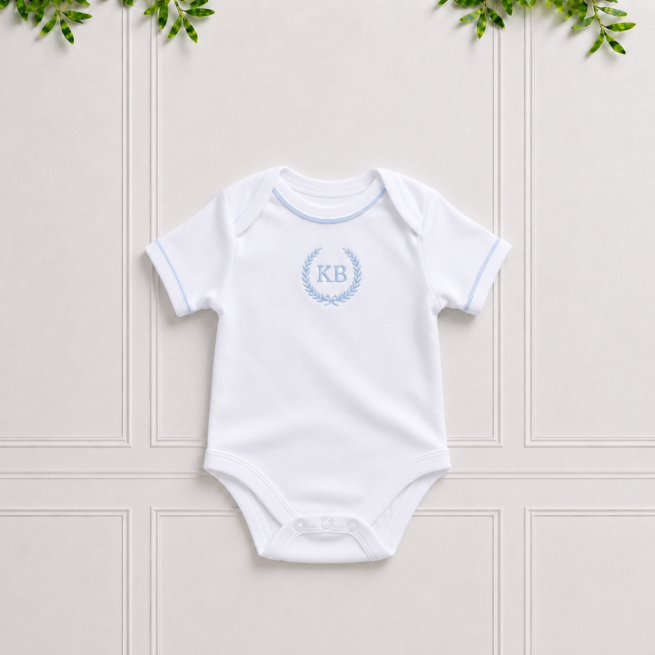 White baby bodyvest in soft cotton interlock with light blue piping, light blue KB embroidery and envelope neckline on a classic Koco Bino background.