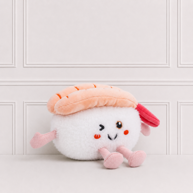 Cute shrimp soft toy with fluffy white body, embroidered winking face and pink legs, displayed on a white surface against a classic panelled backdrop.