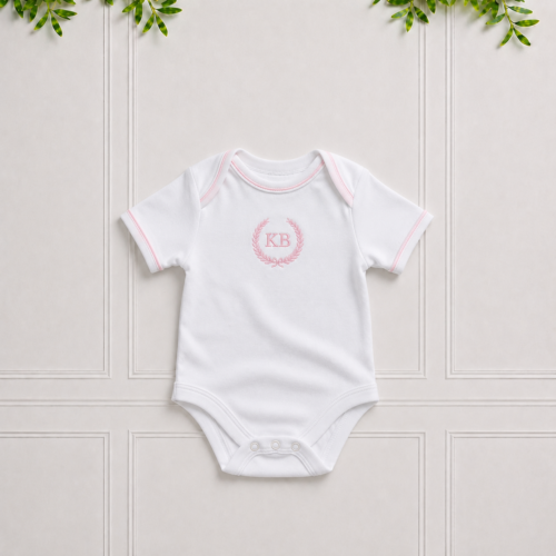 White baby vest in premium cotton interlock with soft pink piping, envelope neckline and elegant pink KB embroidery for everyday comfort.