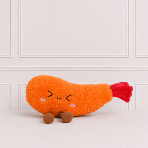 Cute tempura prawn plush toy with embroidered sleeping face and soft orange fabric, sitting on a white surface against a classic panelled background.