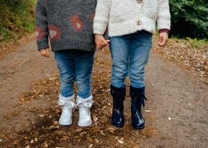 Children wearing white and navy IGOR gumboots with ribbon details while walking outdoors, showcasing stylish waterproof boots for rainy days.