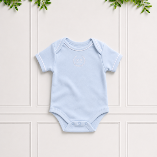 Blue baby bodyvest in soft cotton interlock with envelope neckline, white KB embroidery and white piping, displayed on a classic Koco Bino background.