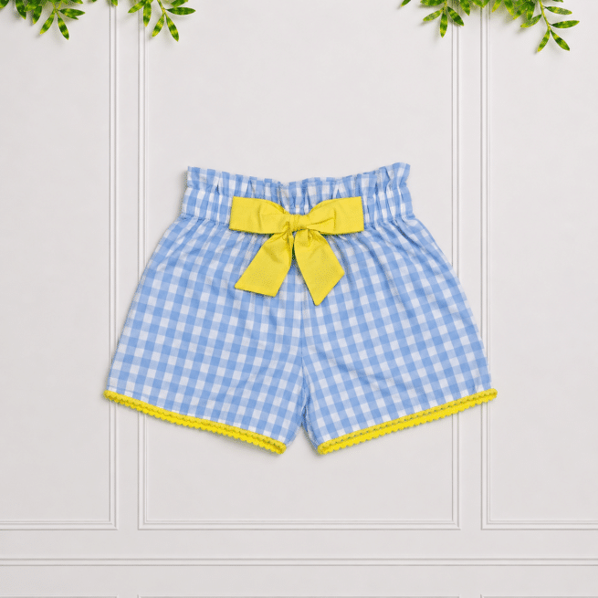 Girls' blue gingham shorts with a yellow bow and scalloped trim, photographed against a white panelled studio background.