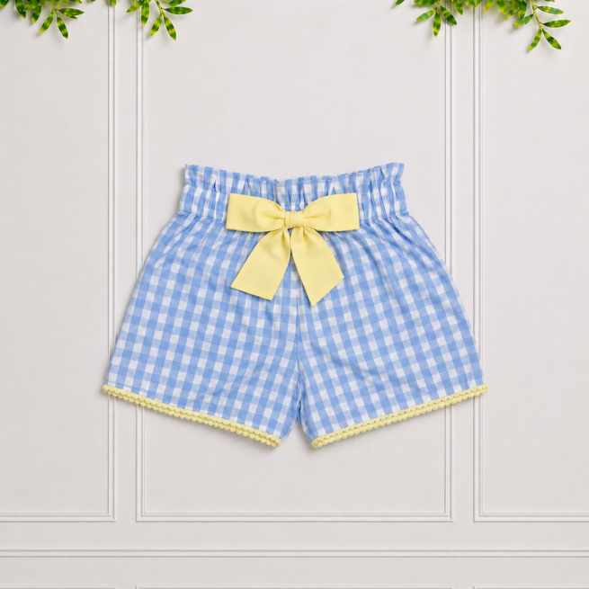 Girls' blue gingham shorts with a yellow bow and scalloped trim, photographed against a white panelled studio background.