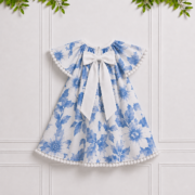 Back view of Emily girls' blue and white floral dress with white pom-pom trim, displayed against an elegant white paneled studio background.
