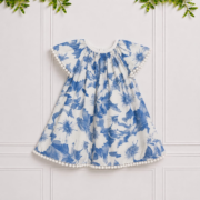 Emily girls' blue and white floral dress with white pom-pom trim and bow, displayed against an elegant white paneled studio background.