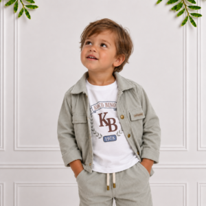 Toddler boy wearing a sage green jacket and matching trousers with a white Koco Bino T-shirt, looking up in a bright, elegant studio setting.