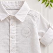 Close-up of a boys white linen shirt featuring a classic collar, button front, rolled sleeve and embroidered