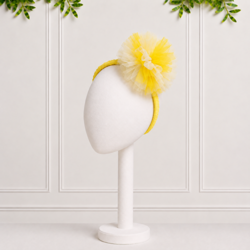 Baby girls yellow headband with a soft tulle pompom detail, perfect for adding a cheerful finishing touch to special occasion and party outfits.