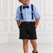 Young boy wearing a light blue KB shirt, black bow tie, black suspenders, black cotton shorts and black loafers in a classic studio setting.