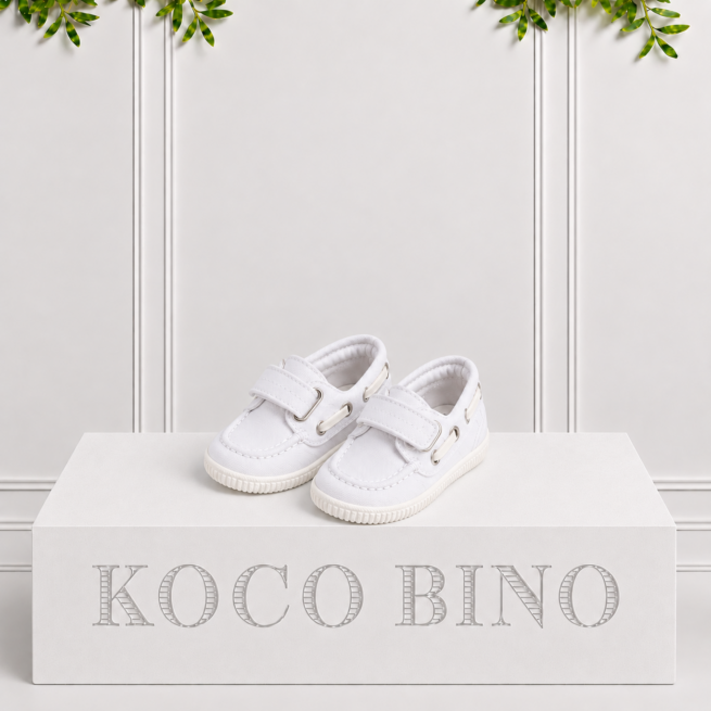 White children's boat shoes with Velcro straps, stitched detailing and textured soles displayed on a Koco Bino branded pedestal against a cream backdrop.