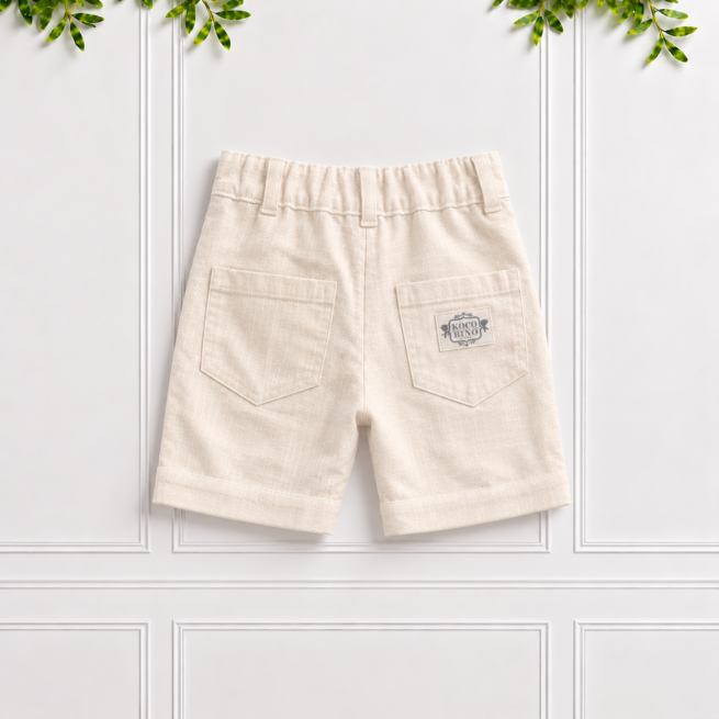 Boys cream linen shorts with back patch pockets, belt loops, elastic waistband and natural linen texture, displayed against a white panelled background.